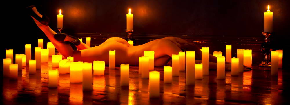 Classy nude figure lying face down surrounded by candles reflected on shinny floorboards