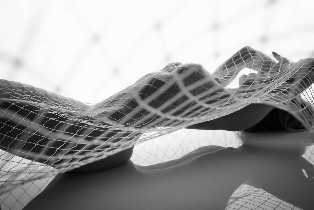 High Key artistic nude on back with fishing net draped over body and stunning reflection